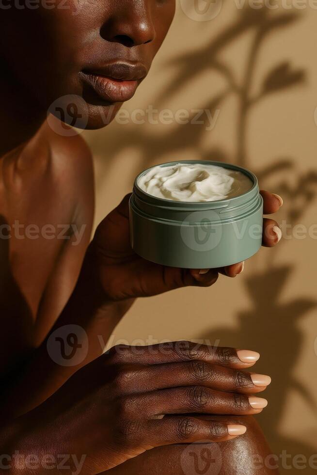 Close-up portrait of a dark-skinned woman holding an open jar of white body cream near her lips, against a warm beige background with soft botanical shadows. photo
