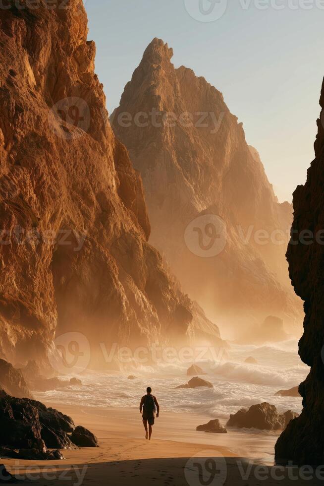 A solitary person with a backpack walks barefoot along a sandy beach framed by towering cliffs and a crashing ocean. photo
