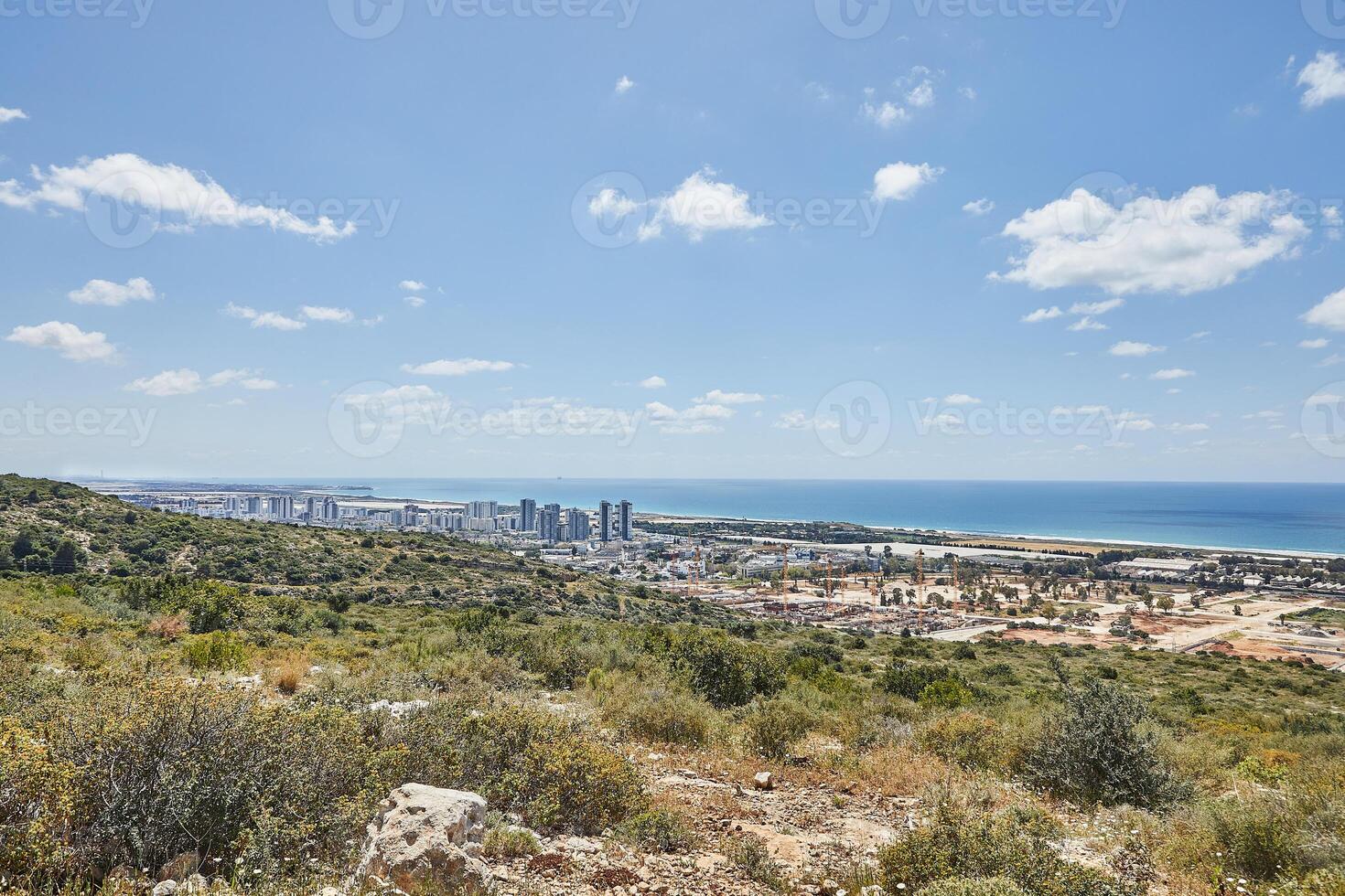 Expansive view of green hills and urban coastline meeting the Mediterranean, under a clear sky with scattered white clouds photo
