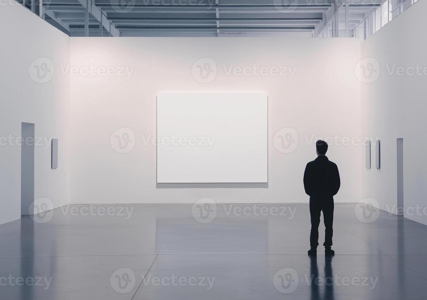 A man stands in a large empty room with a white wall photo