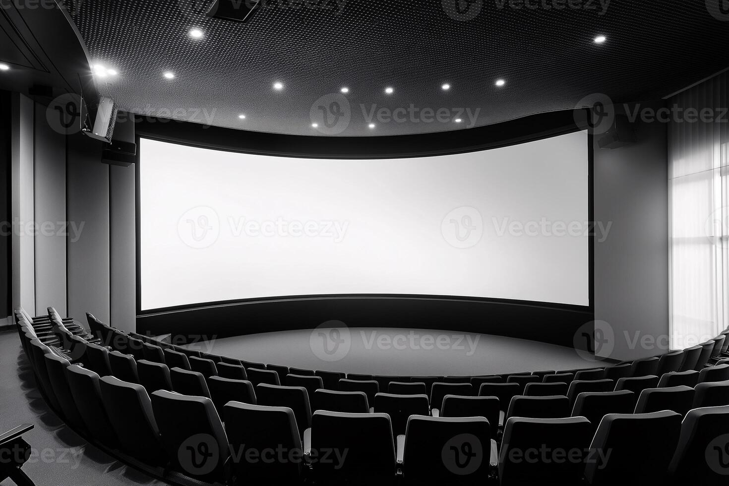 A movie theatre with a large screen and rows of black chairs. photo