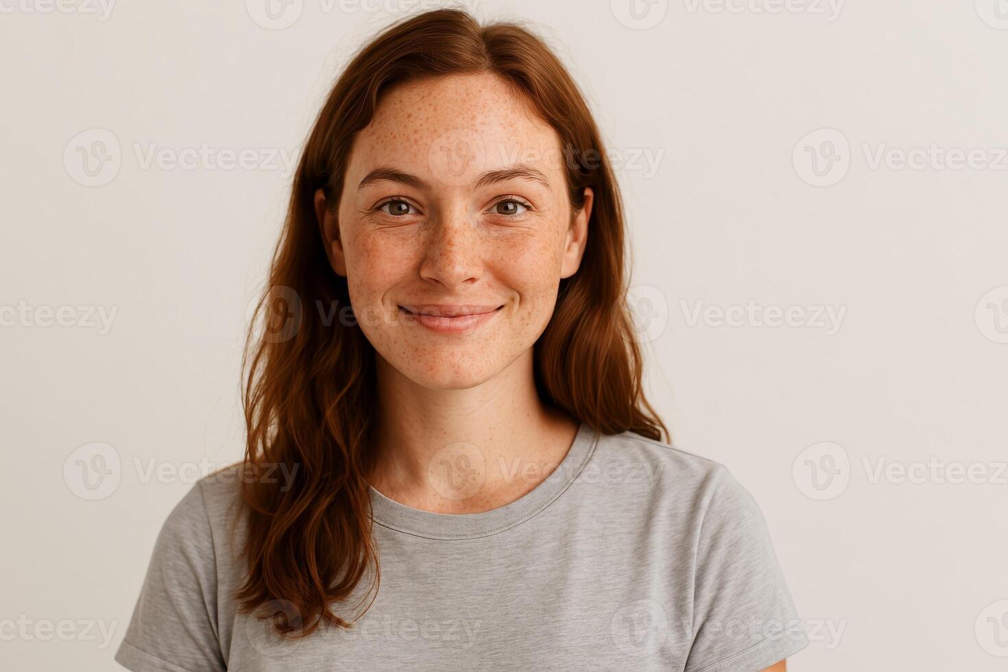 Smiling woman with red hair and freckles wearing gray t-shirt posing in front of neutral background in studio photo