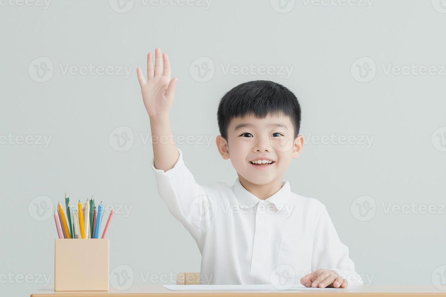 Asian boy raising his hand in front of his desk photo