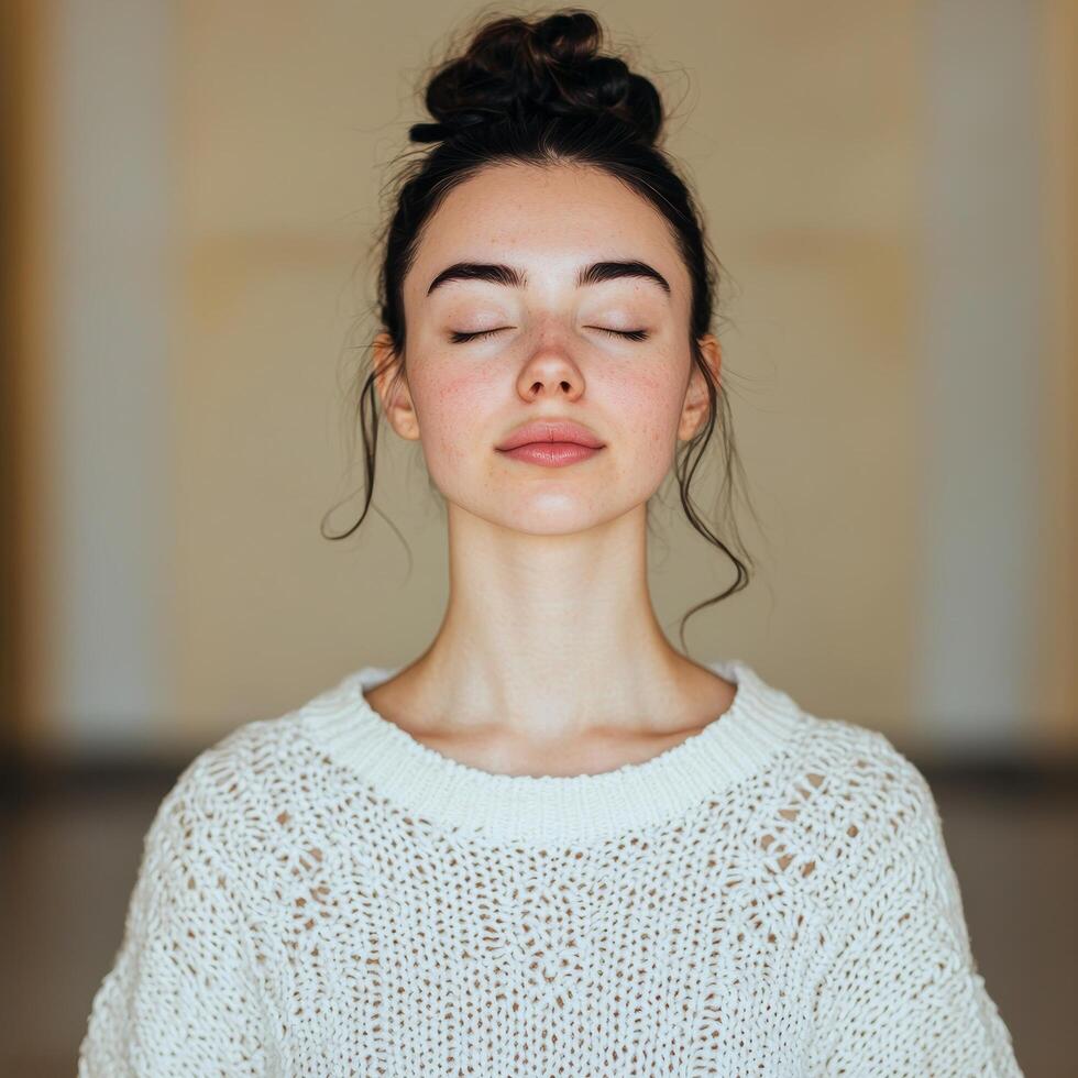 Serene woman in a cozy sweater with closed eyes in soft lighting. photo