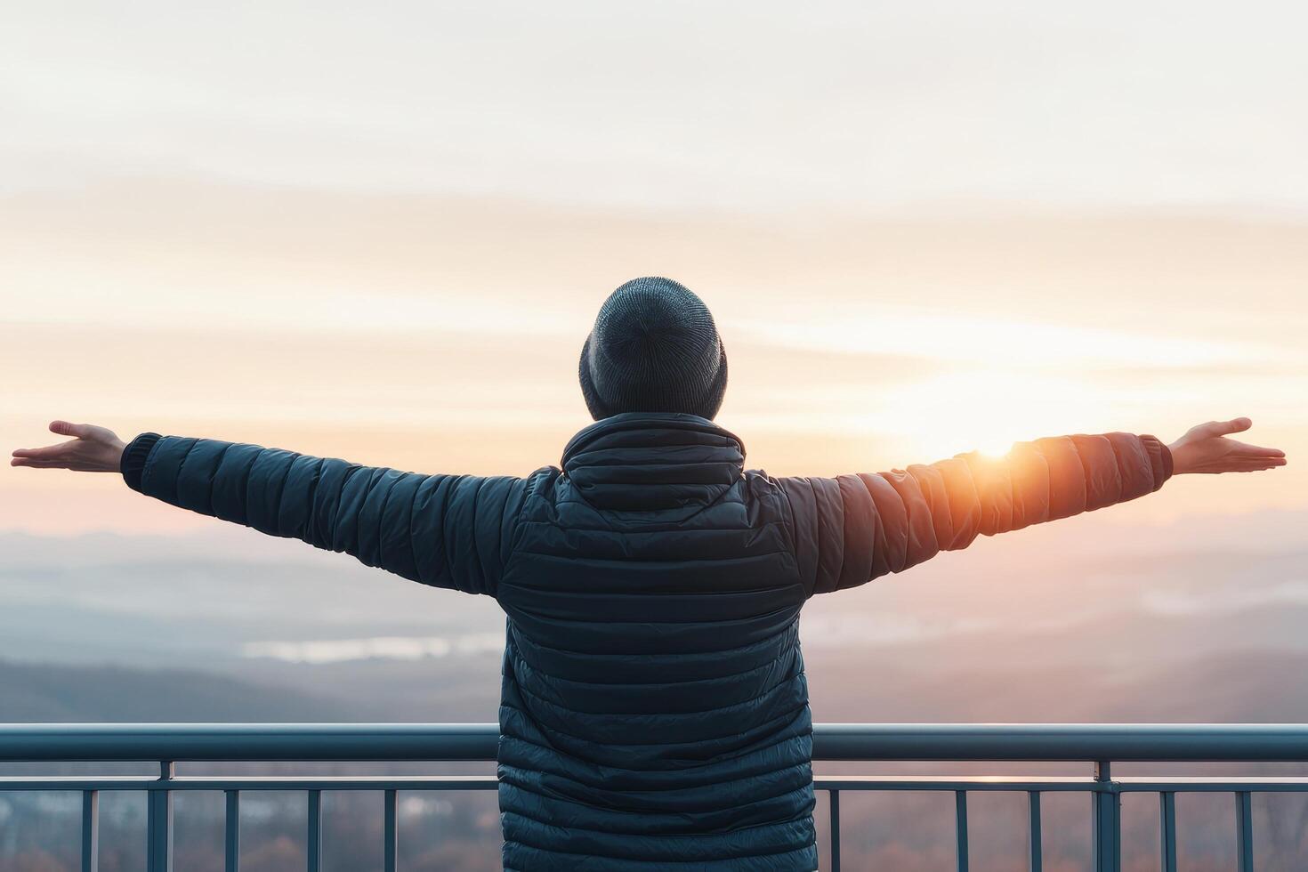 Person with arms outstretched, enjoying a sunrise view from a balcony. photo