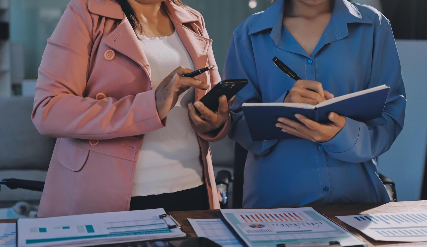 Two women standing at a desk with a notebook and pen photo