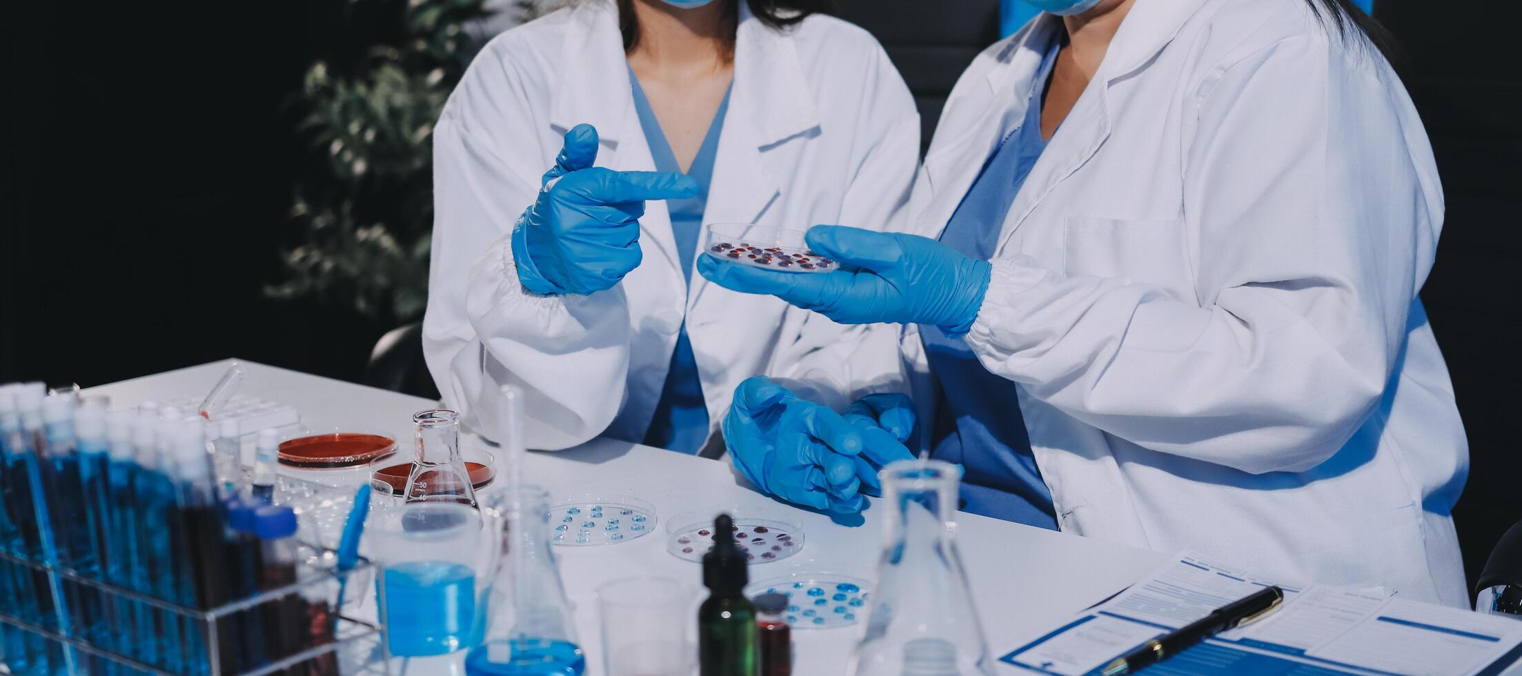 Two women in lab coats and masks holding up a vial photo