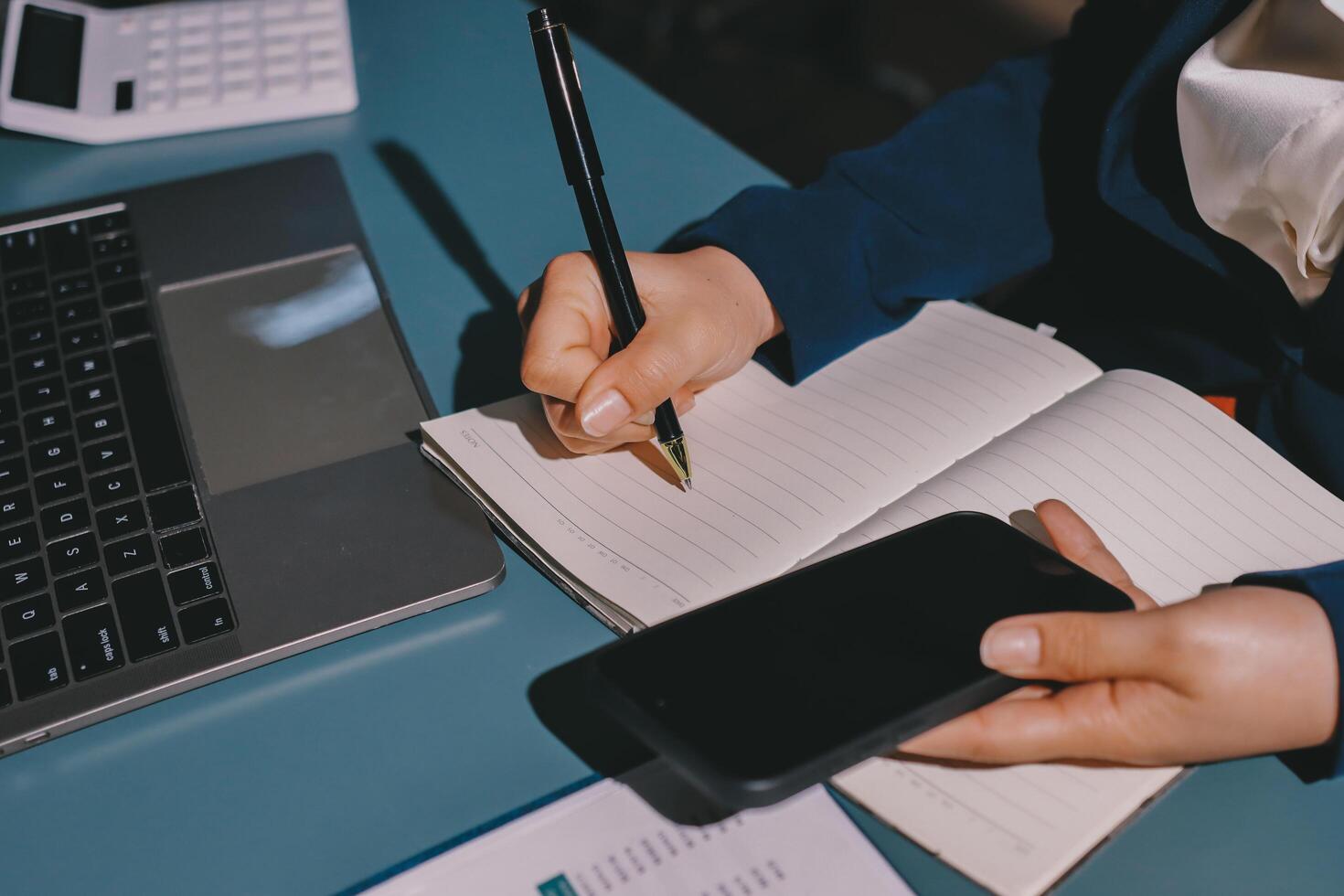 Businesswoman writing on notebook and using smartphone photo
