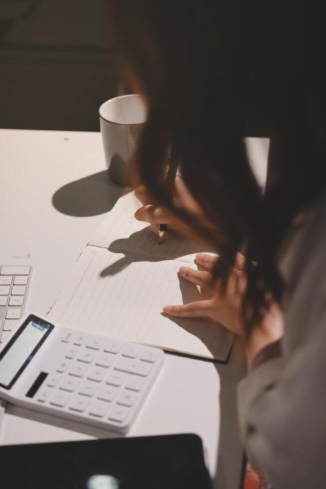 A woman is writing on a notebook with a calculator and a cup of coffee photo