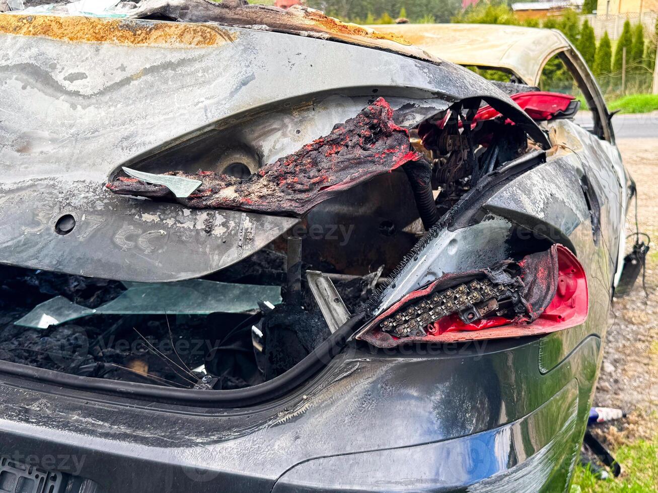 Rear view of a burned car with melted taillights, shattered glass, scorched paint, and extensive fire damage exposing internal components and wiring photo