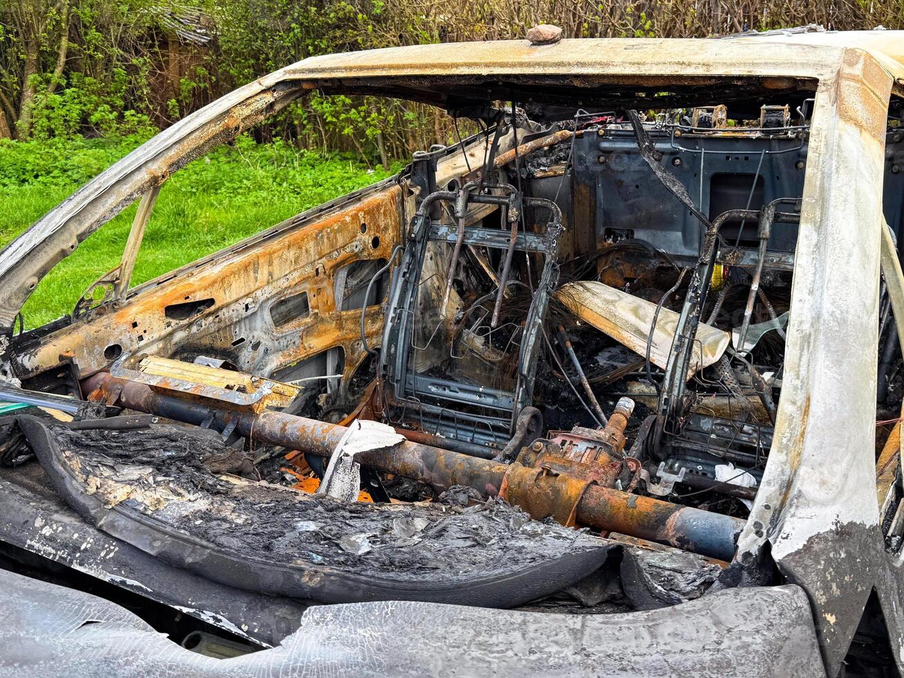 Side view of a completely destroyed car cabin with burnt seats, exposed metal frames, rusted steering column, and ash-covered interior after a severe fire photo