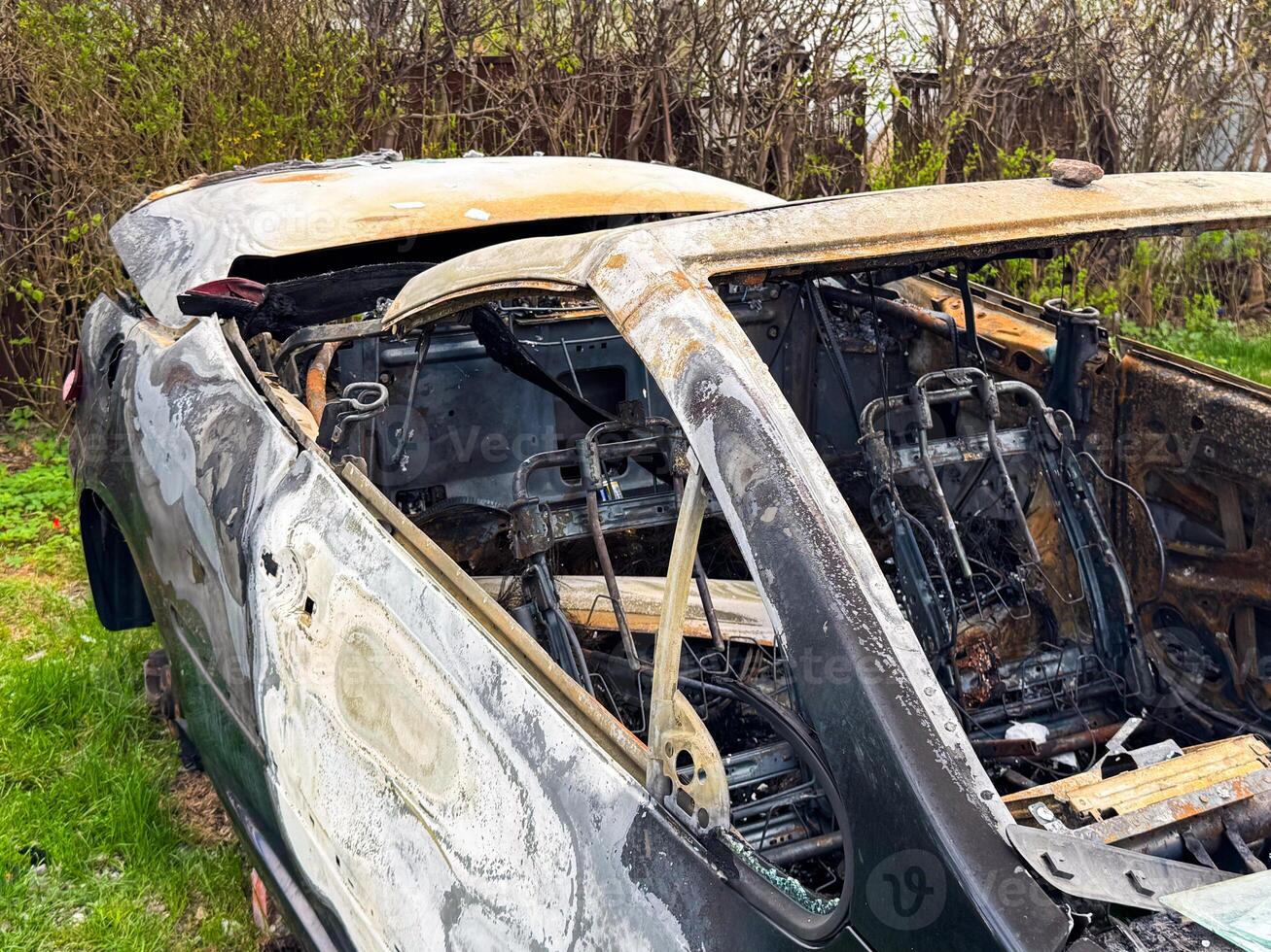 Burned car roof and cabin frame showing heat-warped metal, missing windows, and exposed seat structures after complete fire destruction of the upper body and interior photo