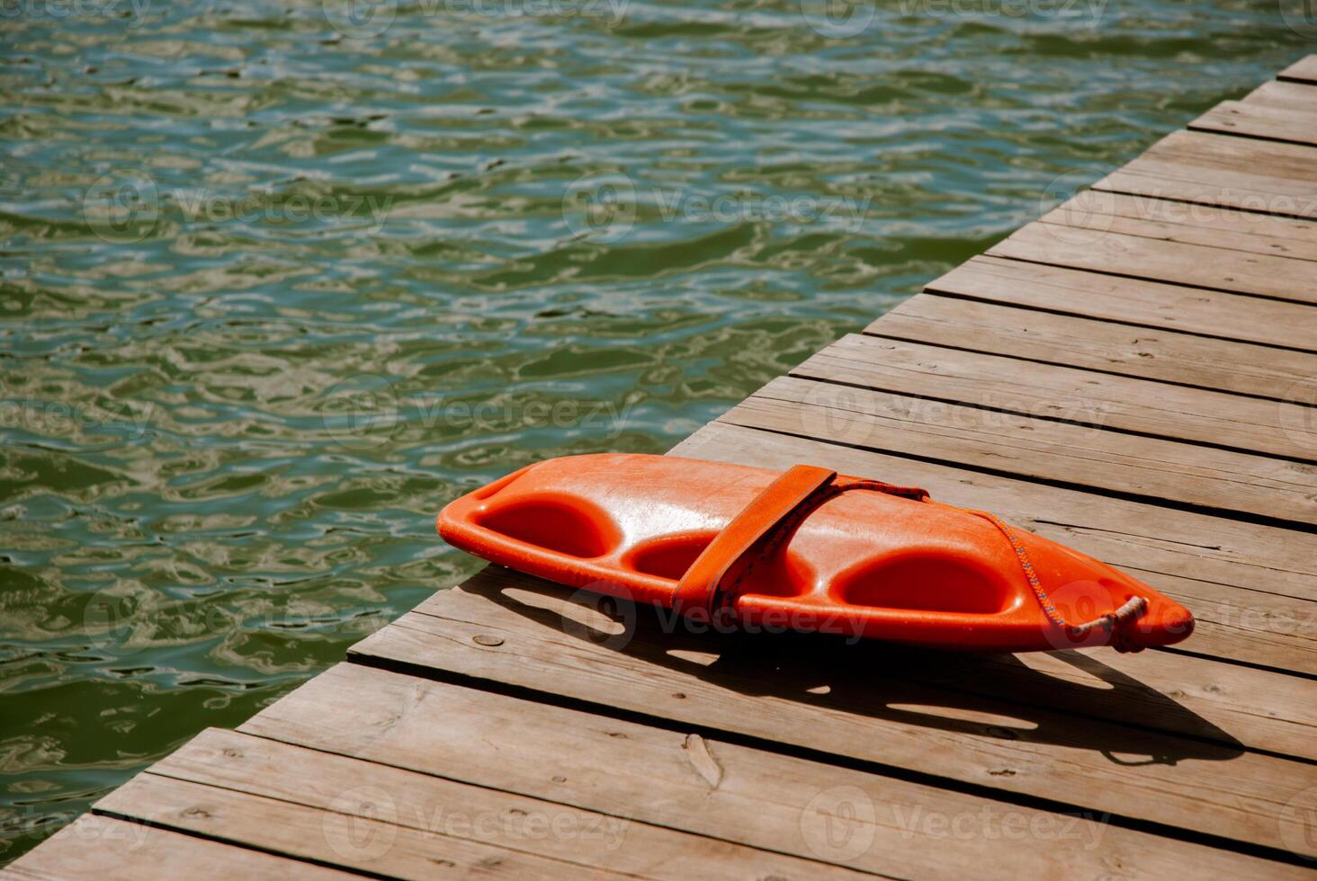 Lifeguard rescue float on wooden dock by lake water surface in summer. Weekend concept near the forest and lake photo