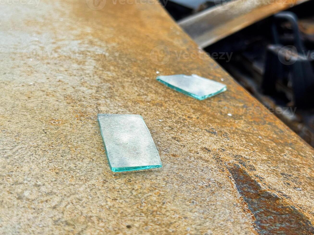 Two flat shards of broken automotive safety glass resting on the rusted hood of a burned car, showing heat discoloration and surface corrosion from fire damage photo