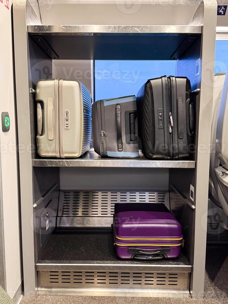 A train luggage rack with multiple modern suitcases in various colors and sizes, neatly organized on two metallic shelves during a daytime journey photo