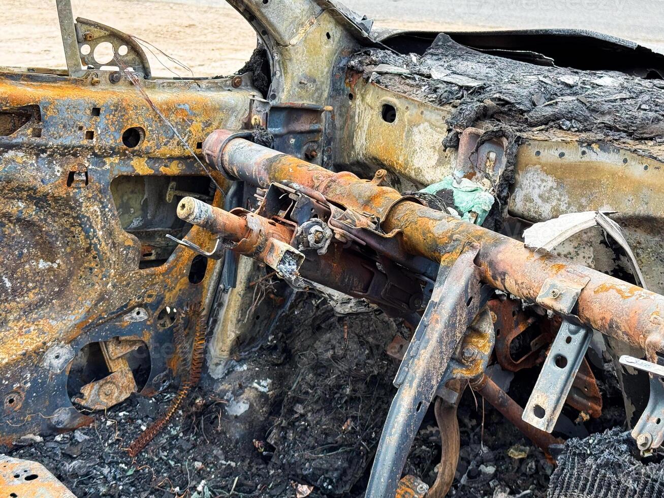 Burned steering column and dashboard frame from a car showing rusted metal structure, melted components, and complete fire destruction of the interior photo