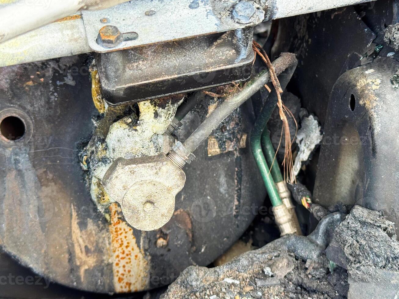 Burned air conditioning compressor valve from a car showing heat damage, melted sealing material, exposed copper wiring, and connected refrigerant lines photo