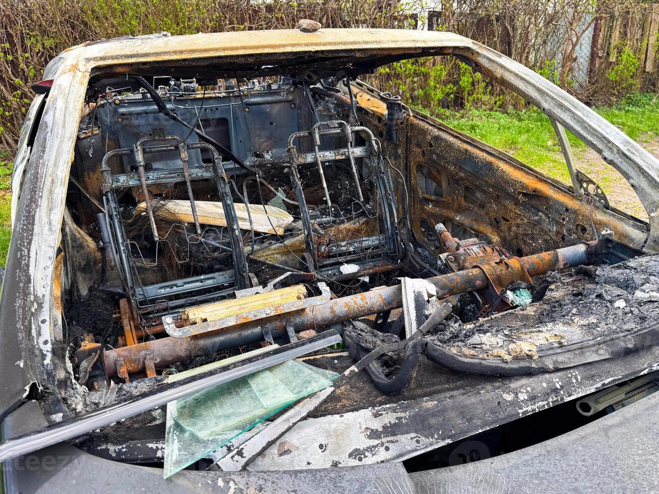 Interior of a completely burned car showing rusted metal frames, charred dashboard, melted components and exposed wires after an intense fire incident photo