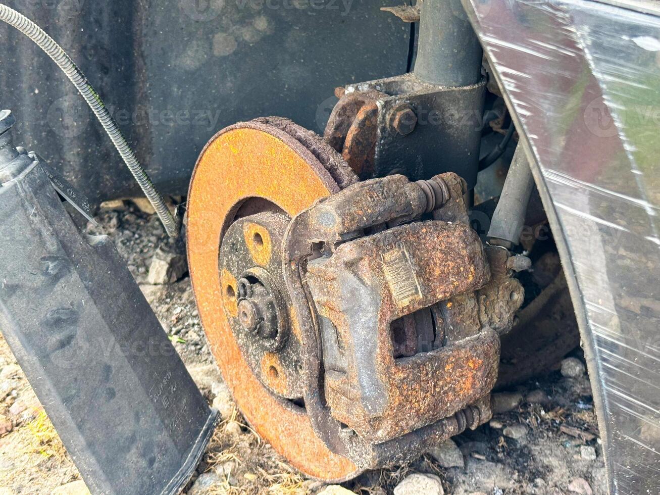 Rusted brake caliper and disc from a car showing severe corrosion on the braking system, with exposed suspension components and wheel hub assembly photo