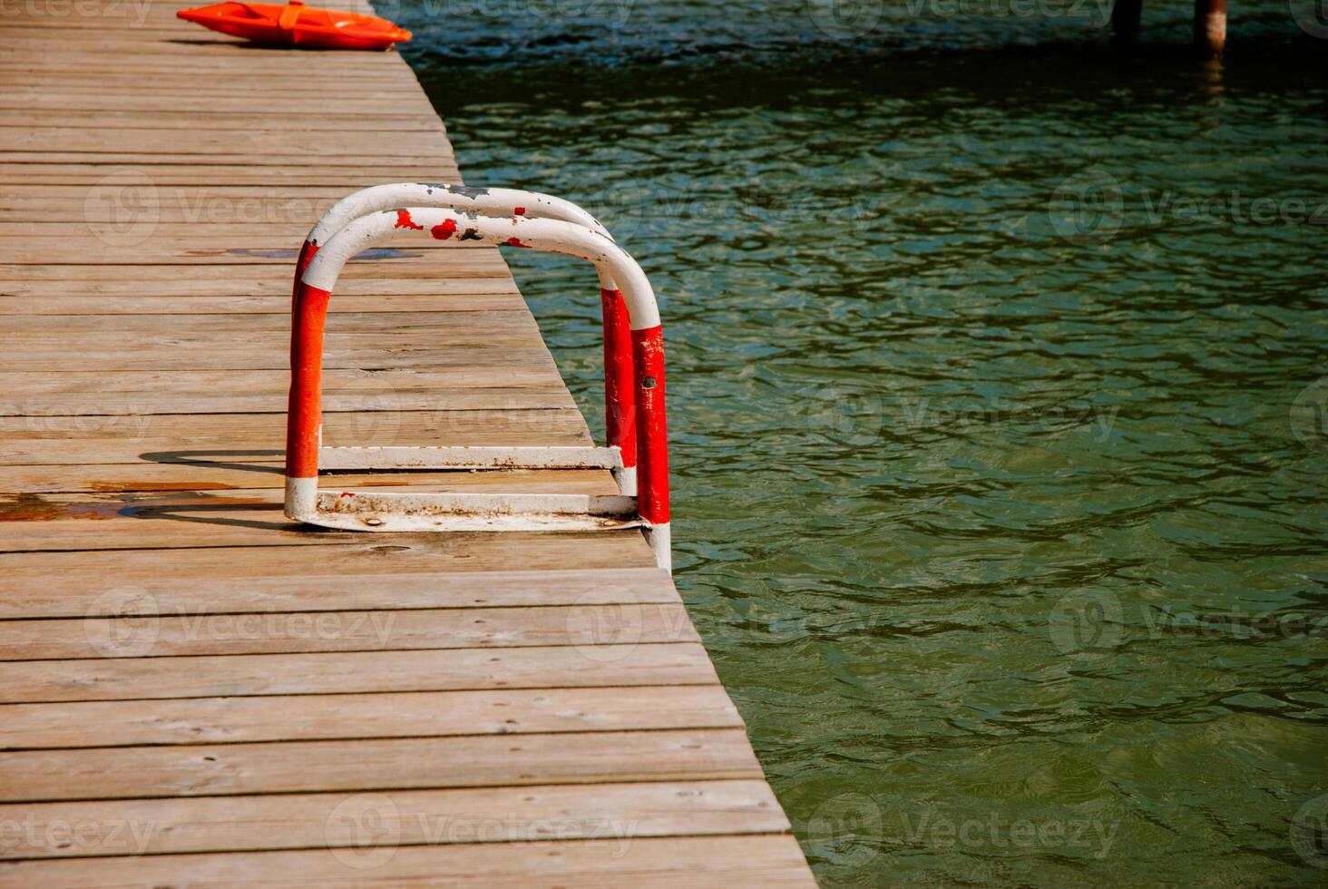 Wooden dock with red white safety ladder by tranquil lake. Weekend concept near the forest and lake photo
