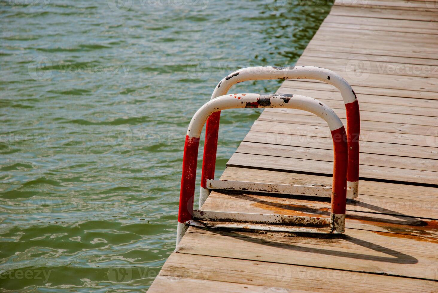 Calm lakeside scene with wooden dock and rusted metal ladder for relaxation and recreation. Weekend concept near the forest and lake photo