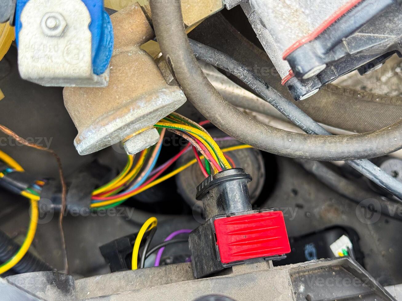 Close-up of a car engine wiring connector with red locking tab and multicolored wires, part of the vehicle's electrical harness located in the engine compartment photo