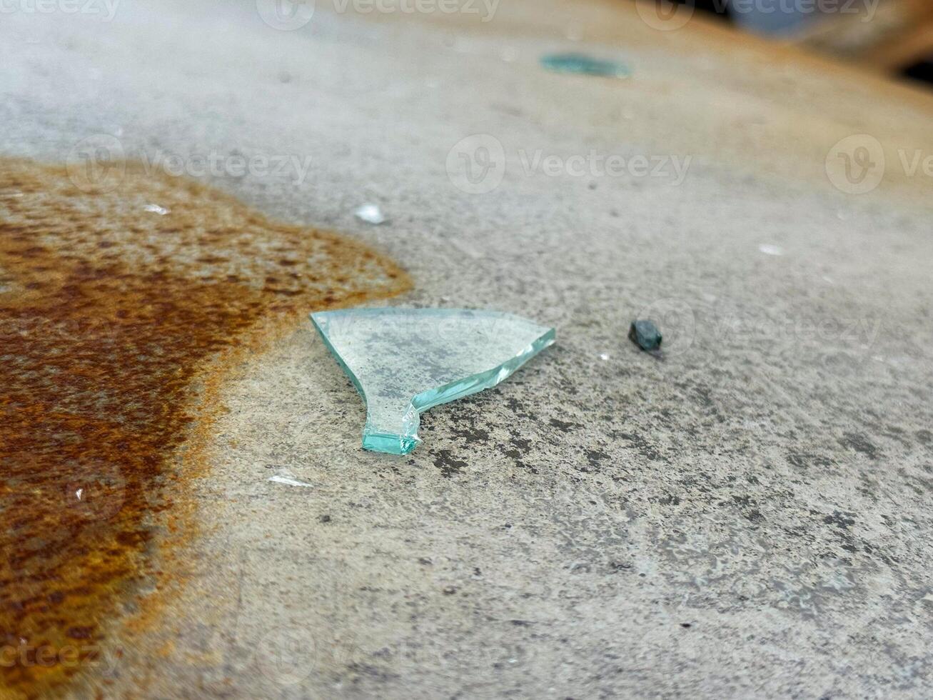 Shard of broken automotive glass on the rusted and scorched roof of a burned car, showing detail of the surface texture and remnants of fire damage photo