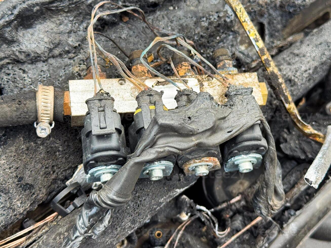 Burned fuel injector rail with connectors from a car engine, showing melted wiring insulation, scorched injectors, and heat-damaged fuel delivery system components photo
