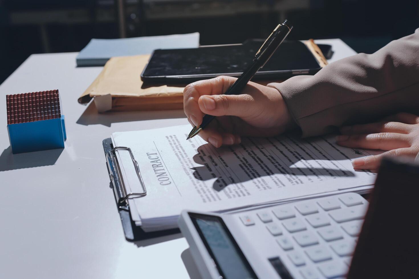A person is writing on a contract with a pen and a calculator photo