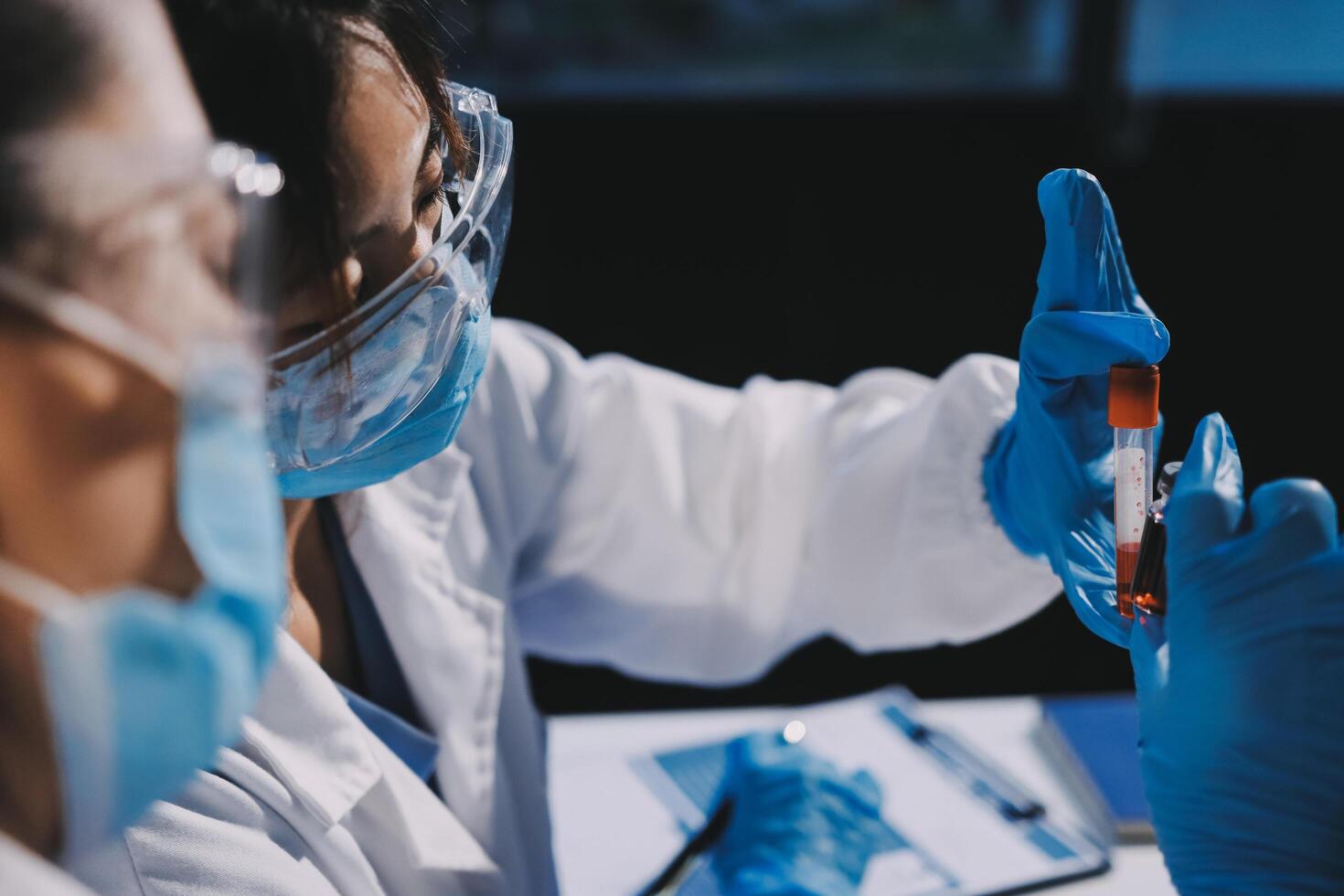 Two people in lab coats and gloves are holding a vial photo