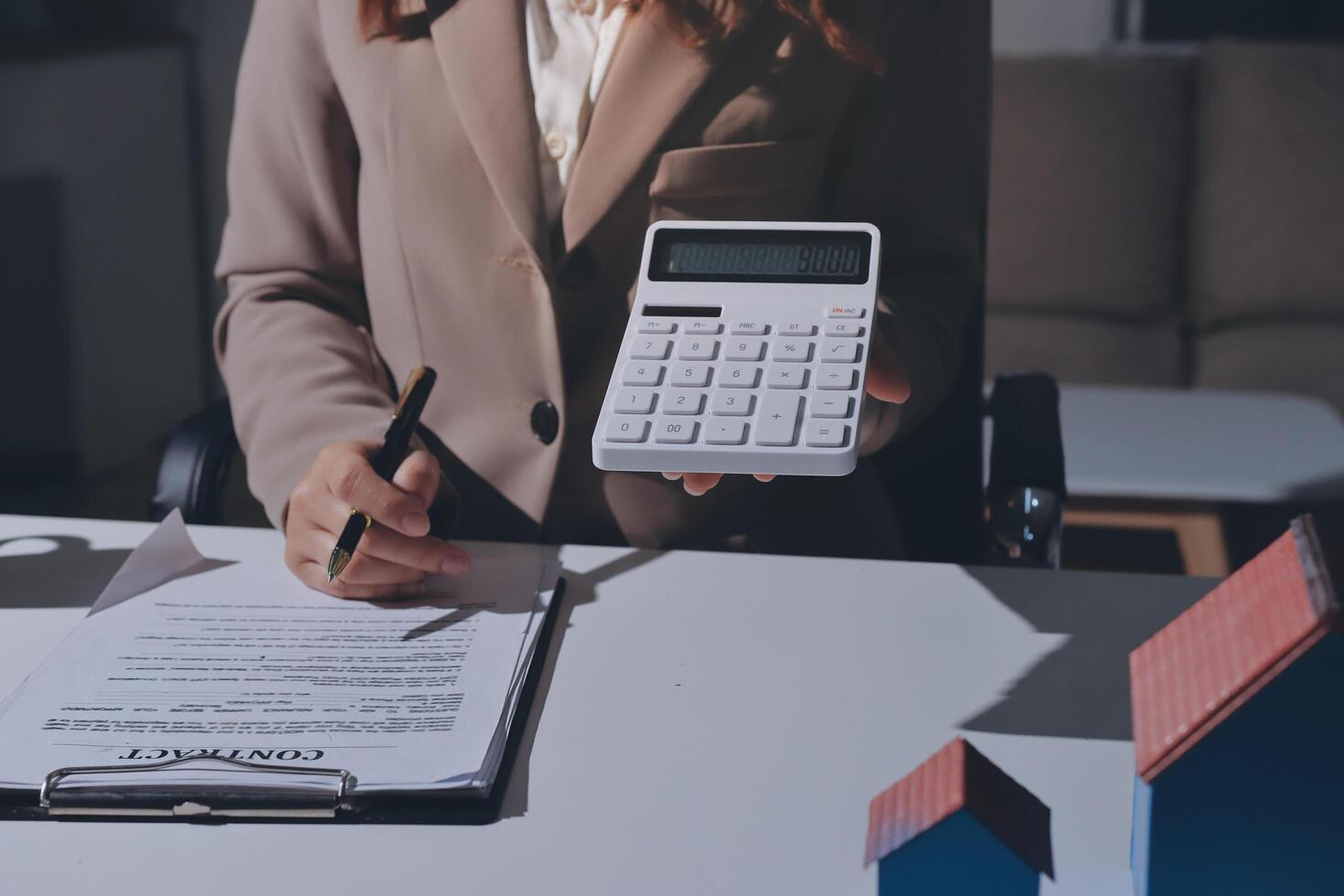 A woman in a business suit is holding a calculator and pen while signing a contract photo
