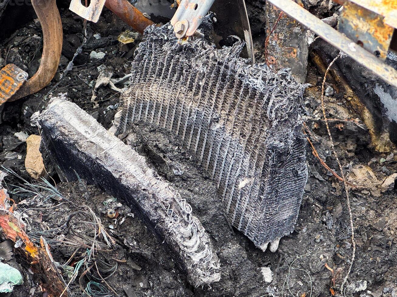 Burned heater core from a car showing severe fire damage, melted fins, and exposed internal structure lying among charred debris and wiring remnants photo