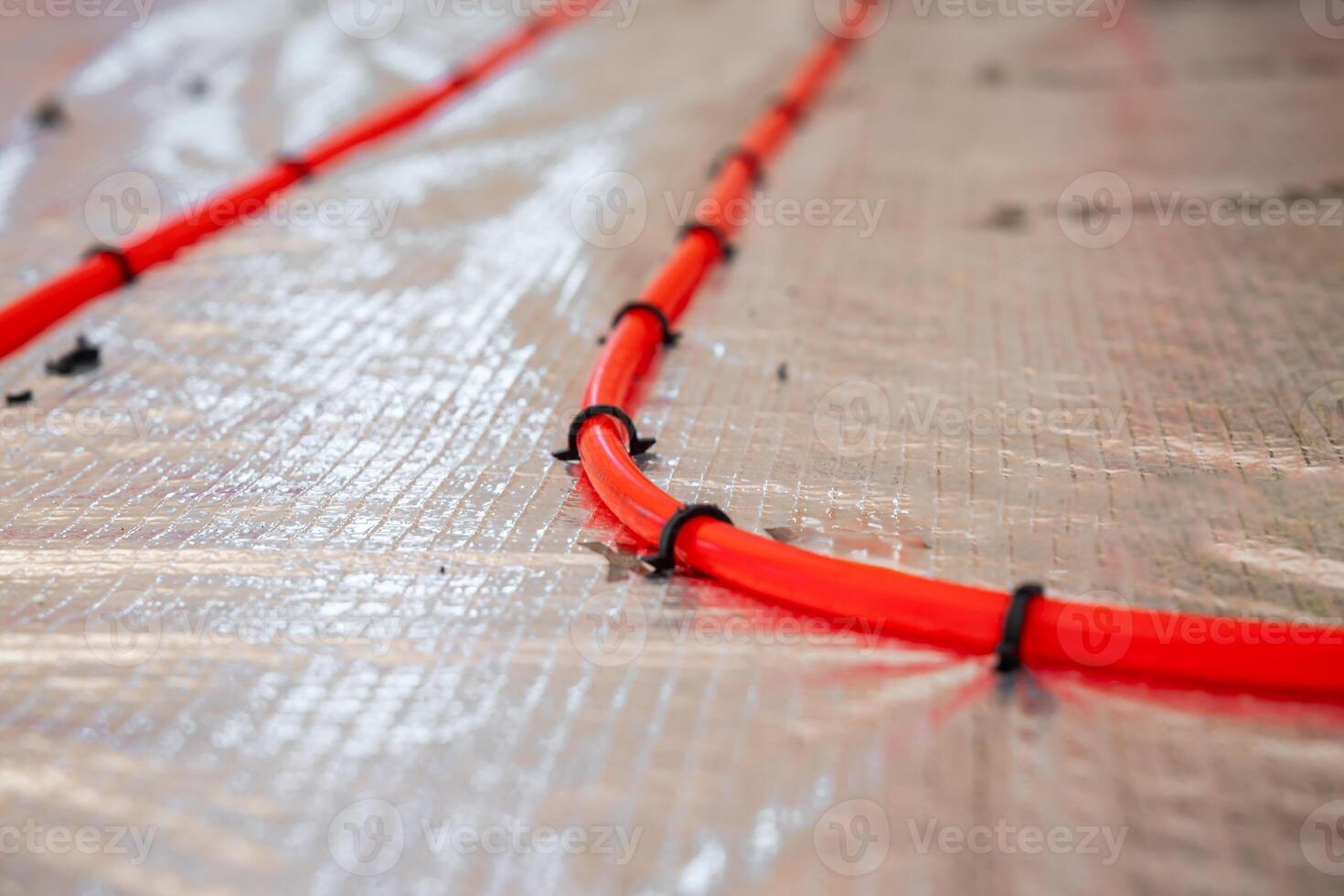 Bright red underfloor heating pipes arranged in curves, secured with black clips on reflective foil insulation, prepared for Estrich concrete layering. photo
