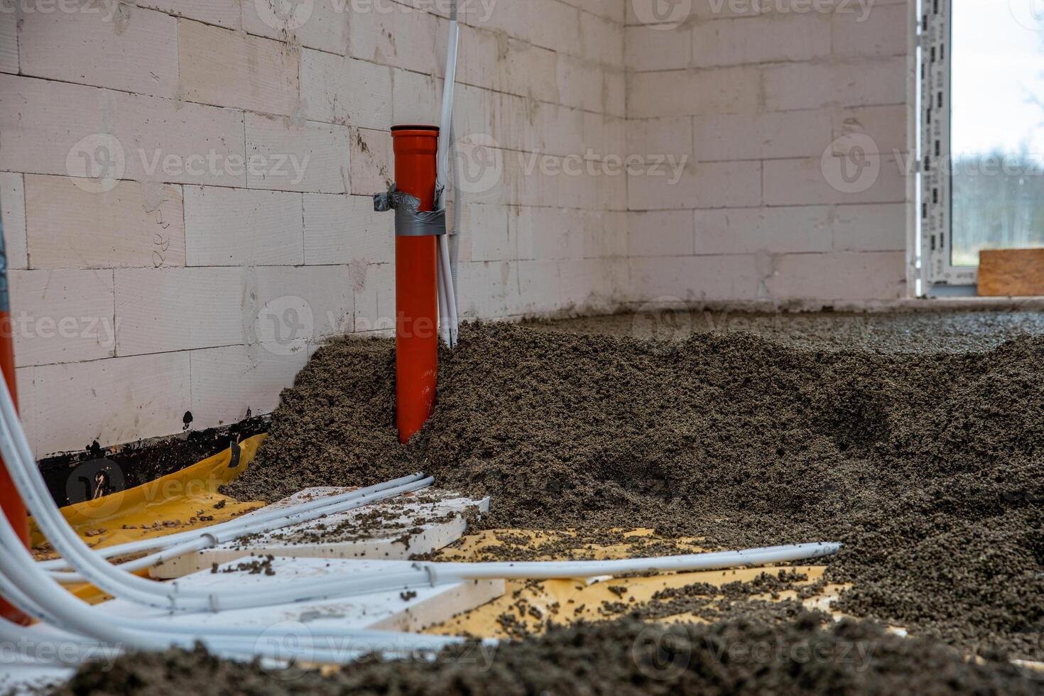 Interior of a construction site with white concrete block walls, an orange pipe taped to the wall, and conduit pipes on a floor of loose aggregate. photo