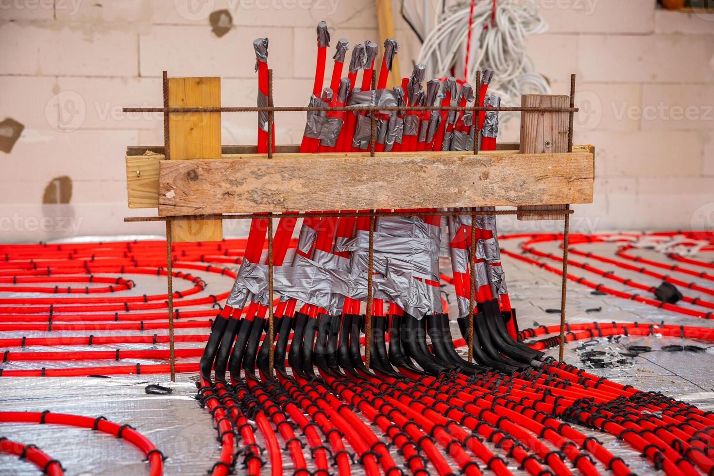 Red and black pipes arranged systematically on a reflective surface, secured with duct tape, with coiled wires and a partially finished wall visible. photo