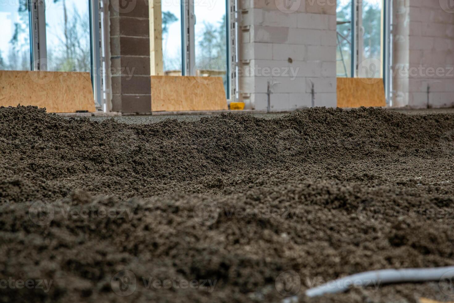 Construction site showing a gravel or concrete floor, white block walls, large metal framed window openings, and wooden boards at the base. photo