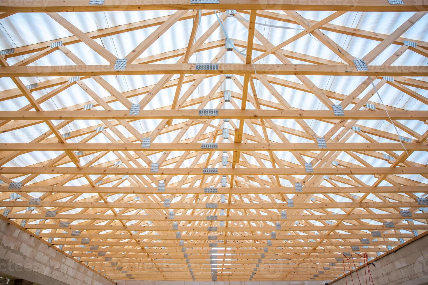 Detailed view of a wooden truss roof structure under construction, featuring light through translucent panels and unfinished concrete block walls below. photo