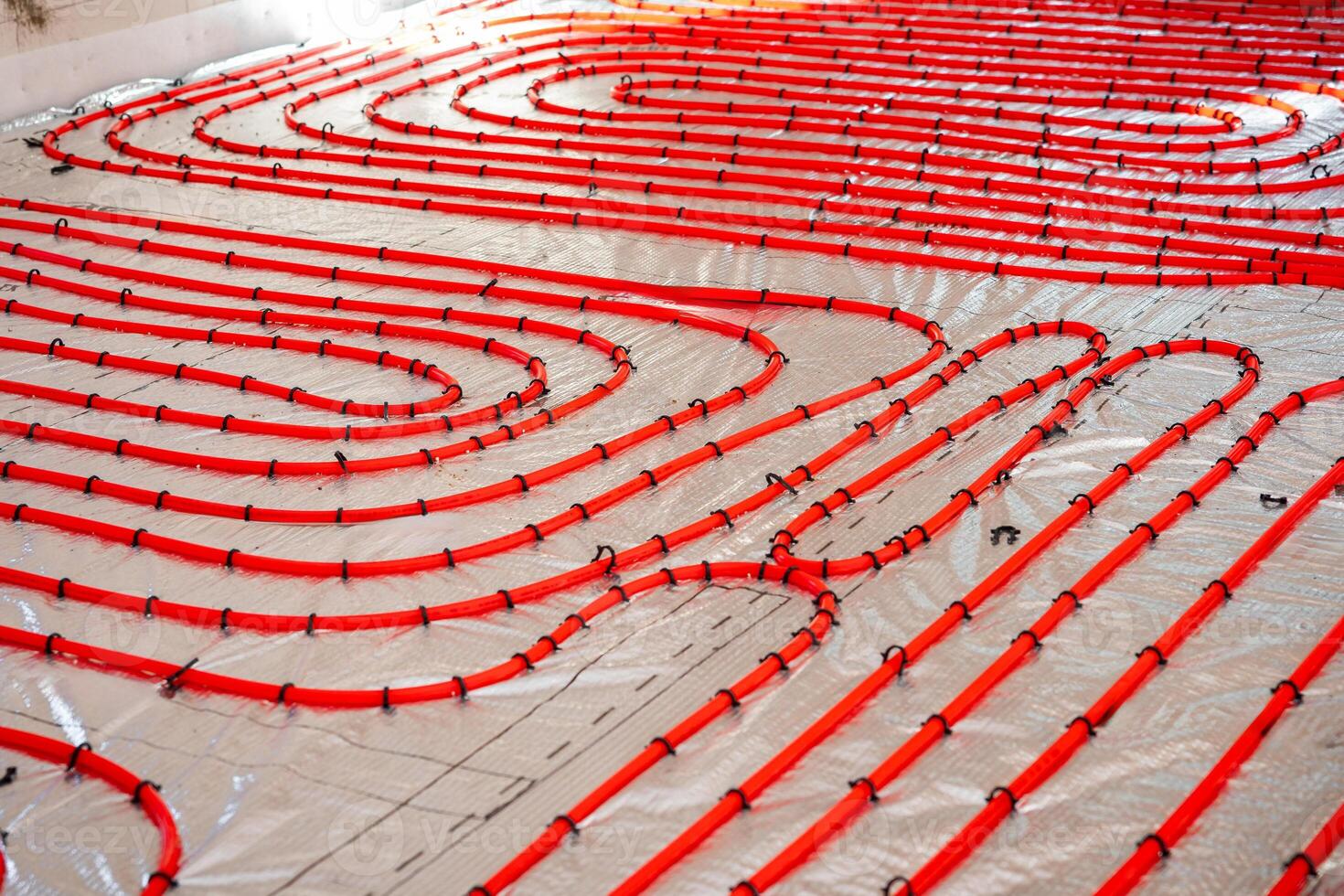 Bright red underfloor heating pipes secured with black clips on a silver reflective surface, prepared for concrete application in a construction project. photo