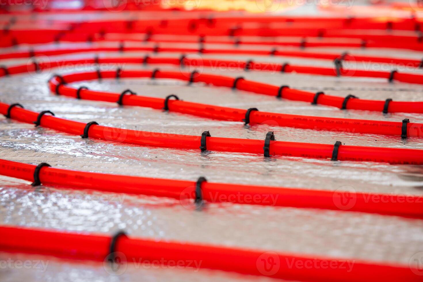 Red underfloor heating pipes arranged in a curved pattern, secured with black clips on a reflective surface, prepared for Estrich concrete application. photo