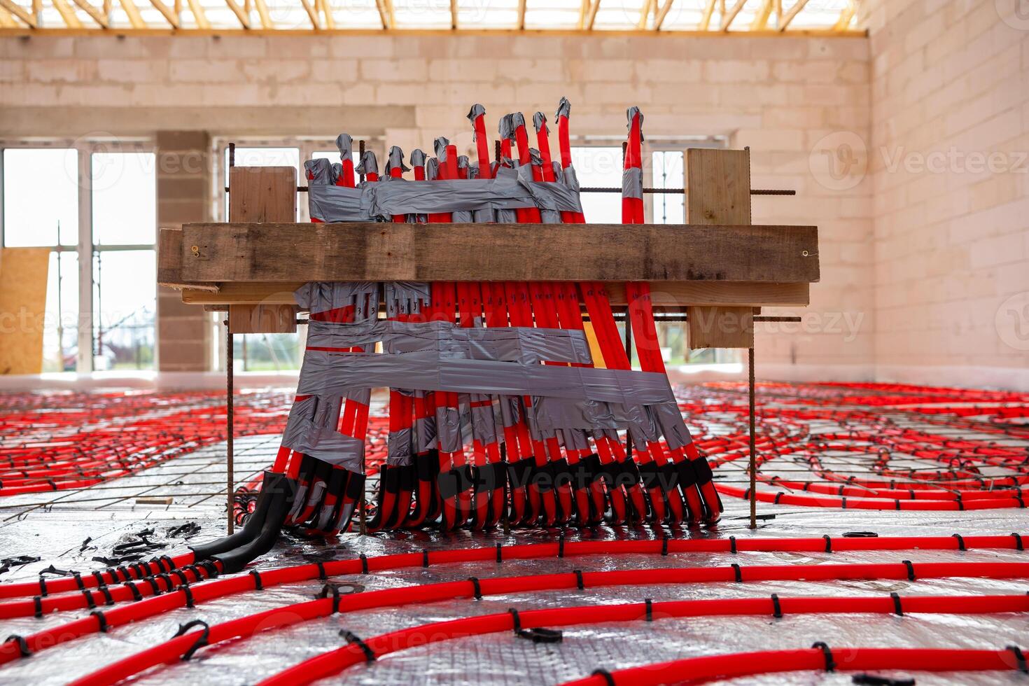 Construction site interior showing underfloor heating pipes in a grid pattern, light brick walls, exposed wooden beams, and natural light illumination. photo