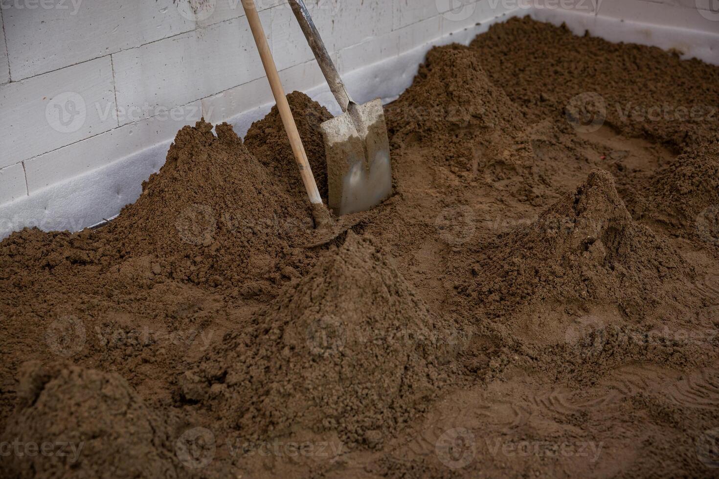Interior of a construction site with sand spread on the floor, tools against a white brick wall, and visible marks indicating active preparation work. photo