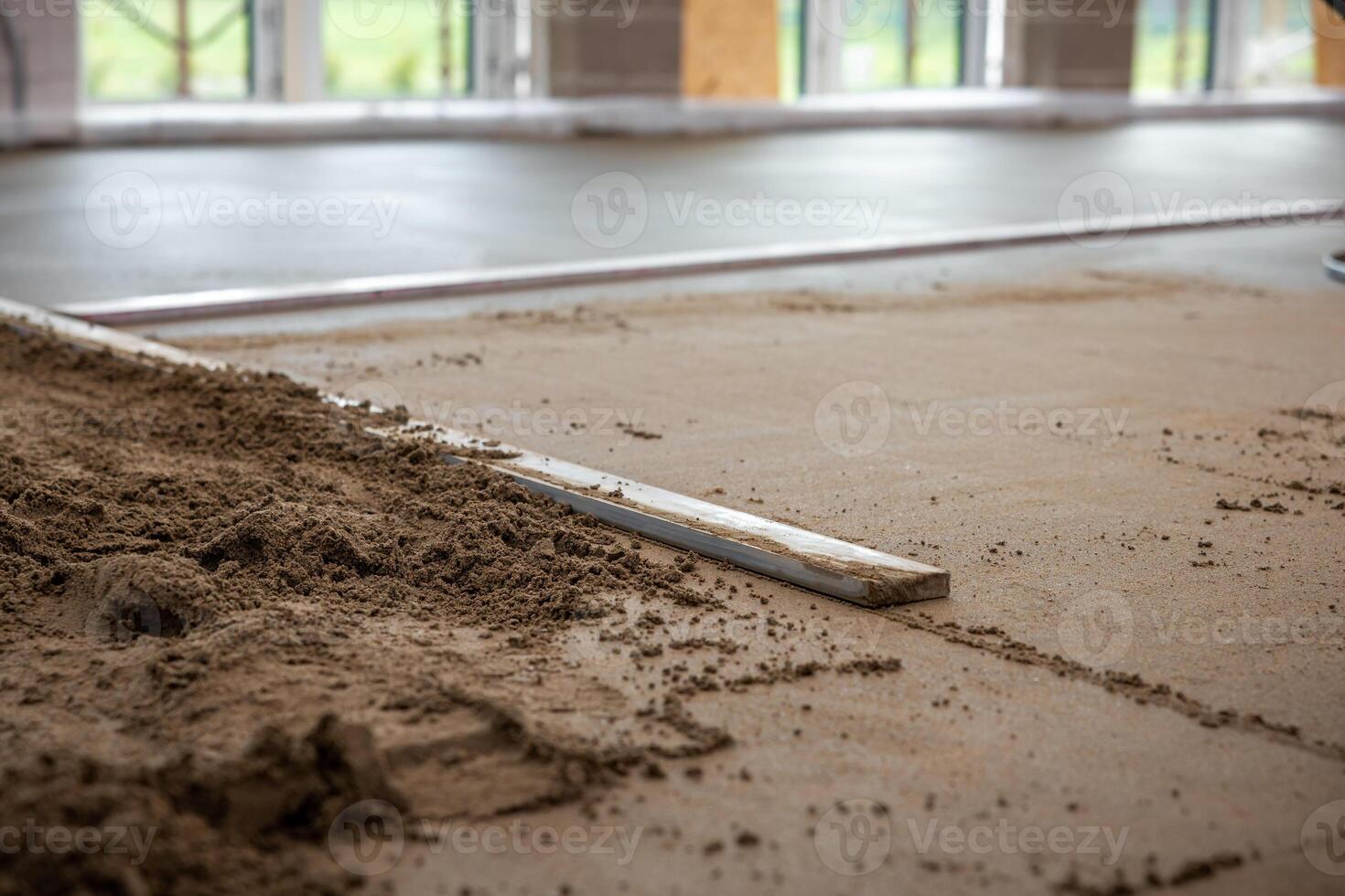 Construction site interior showing underfloor heating pipes being installed and covered with screed concrete. Natural light enters through large windows. photo