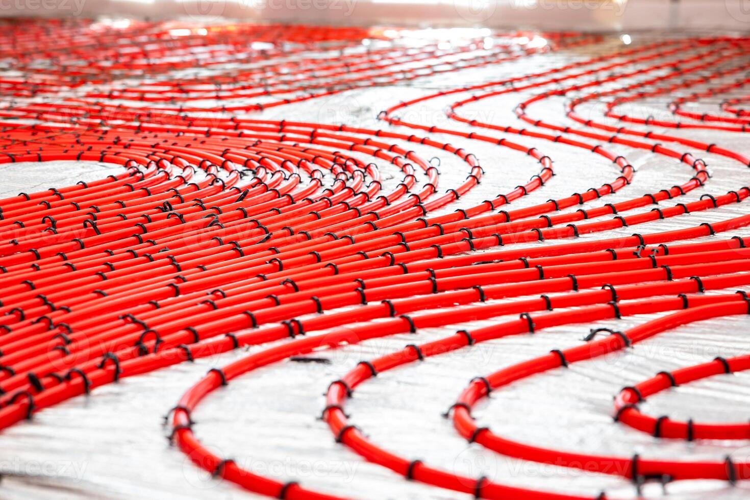 Red underfloor heating pipes arranged in curved patterns, secured with black clips on a light surface, prepared for Estrich concrete application. photo