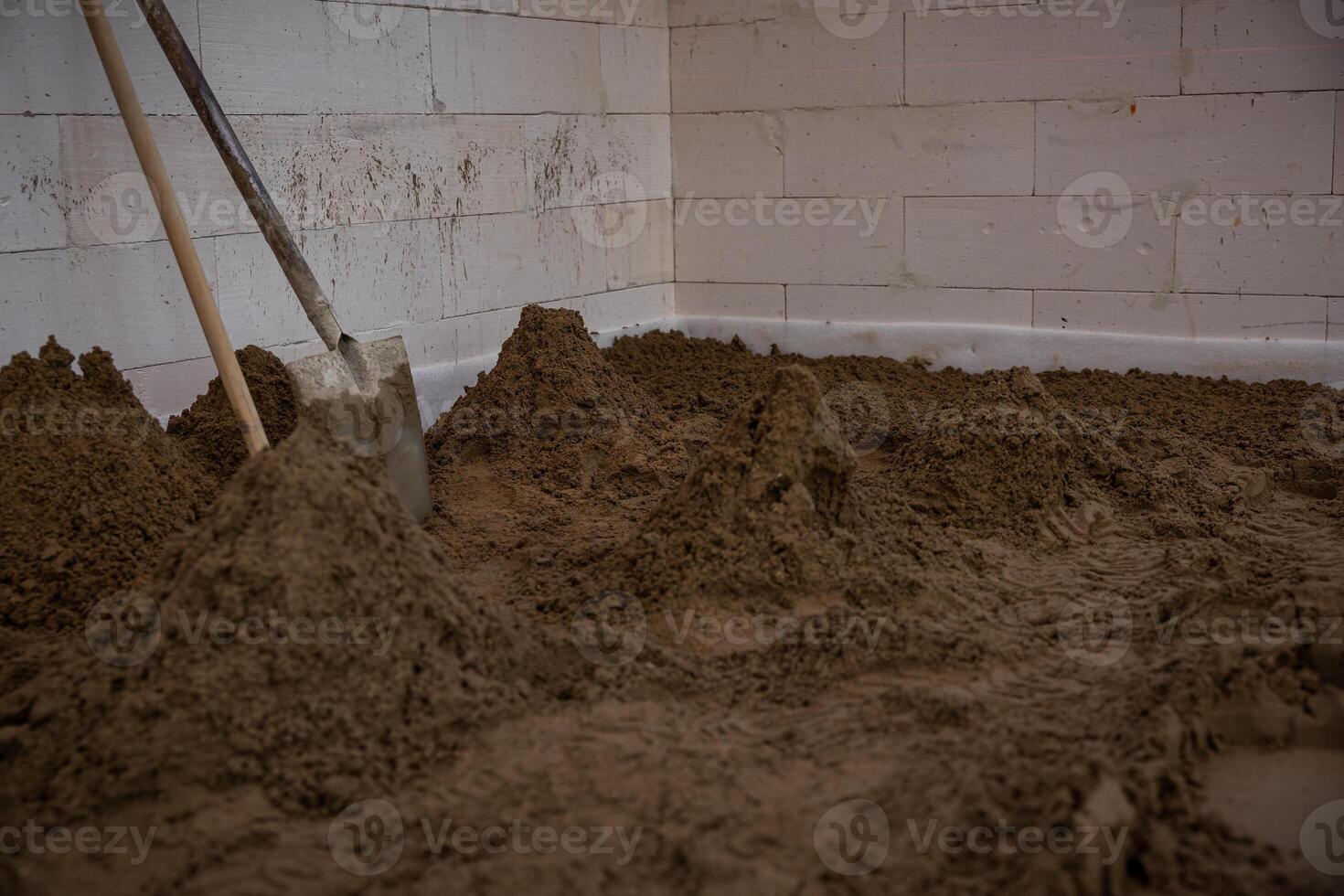 Interior of a construction site with sand piles on the floor, a shovel against white block walls, and visible signs of ongoing work. photo