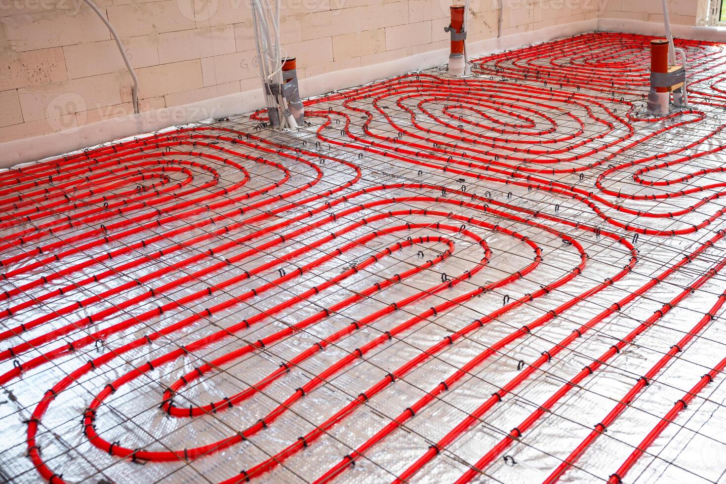Interior of a construction site showing red underfloor heating pipes arranged in a spiral pattern on a metallic mesh over reflective insulation. photo
