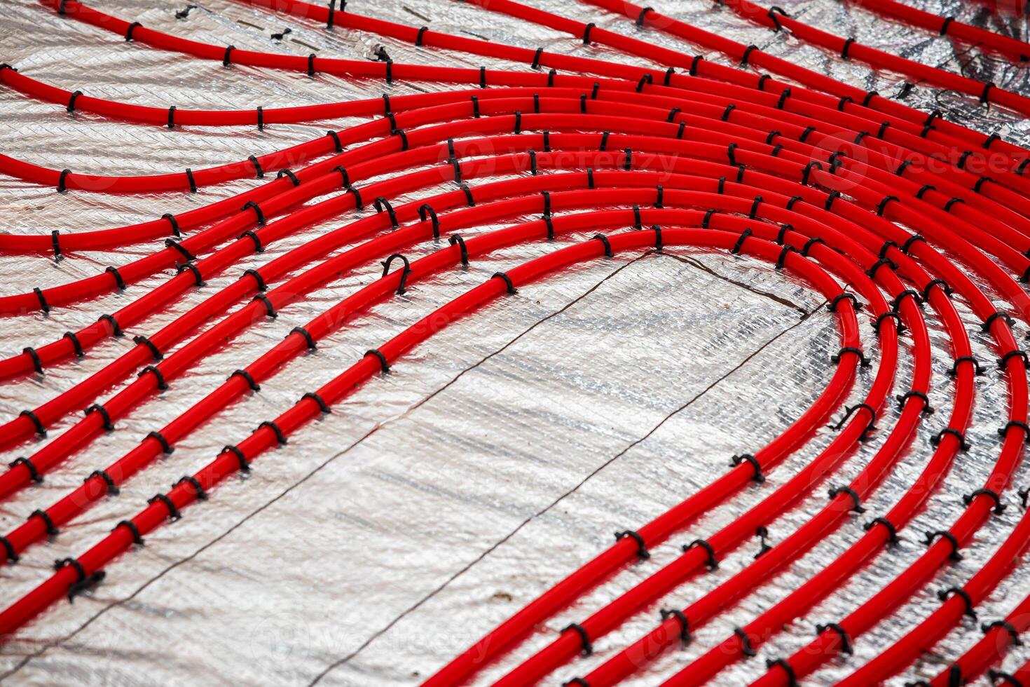 Curved red underfloor heating pipes secured with black fasteners over reflective foil insulation, prepared for a concrete layer in a construction process. photo