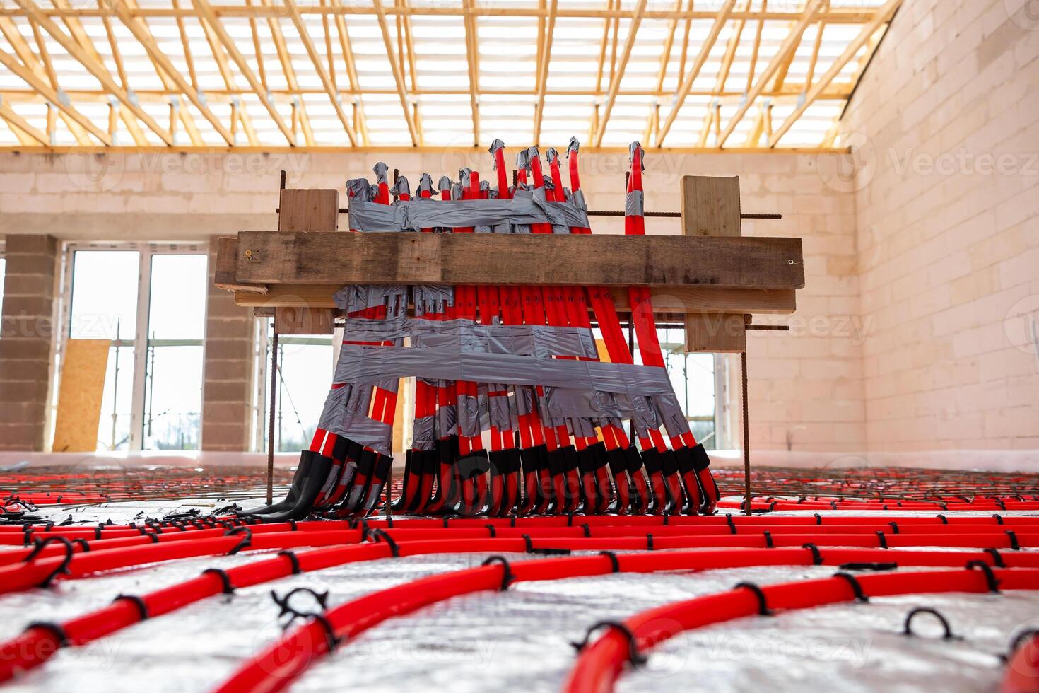 Interior of a construction site with red underfloor heating pipes in a grid pattern, secured to a wooden frame. Exposed beams and brick walls are visible. photo