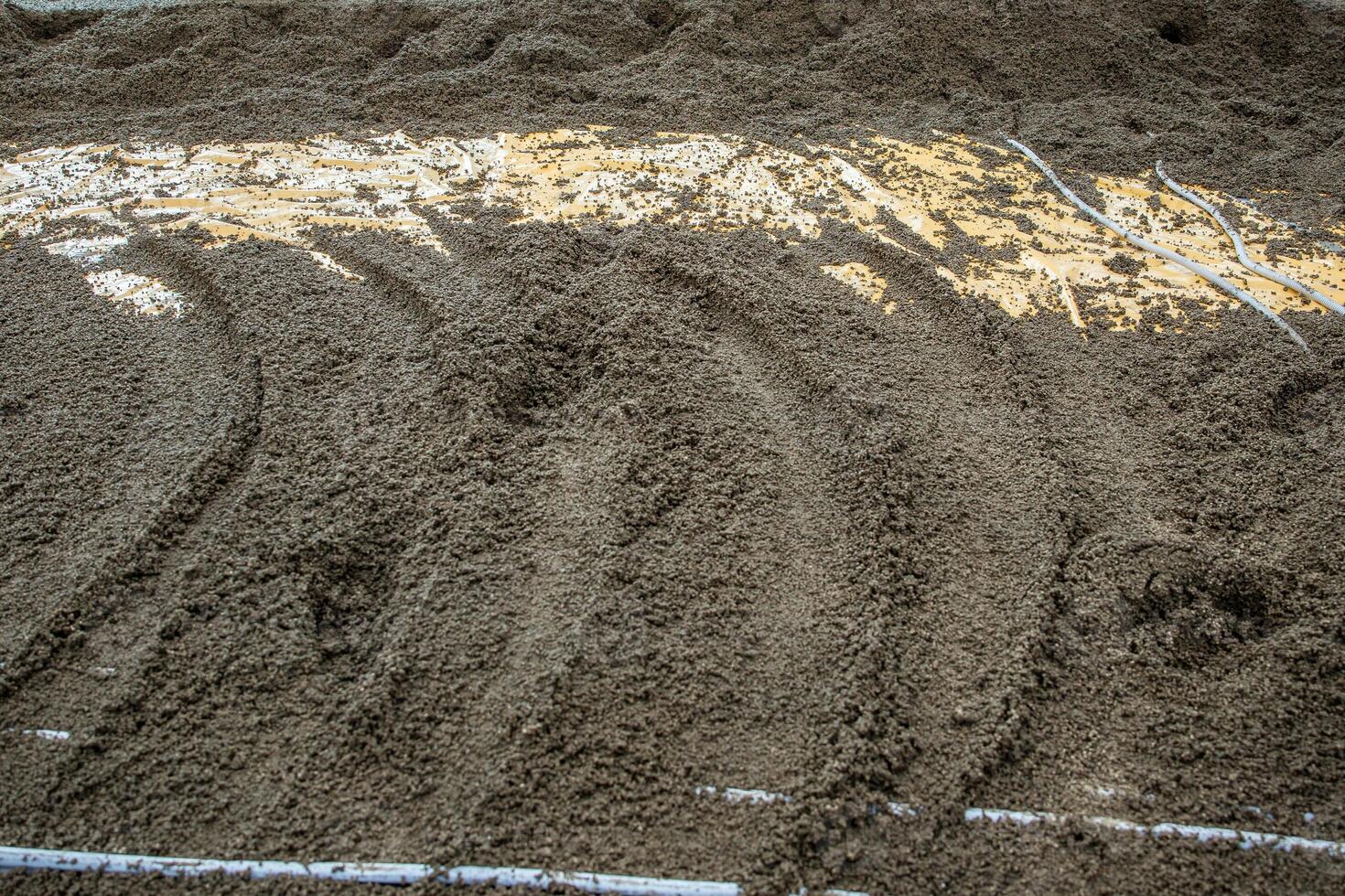 A detailed view of wet cement or sand with grooves, exposed yellow material, and embedded white pipes, indicating a construction process. photo