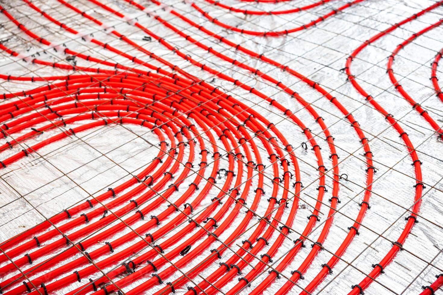 Detailed view of red underfloor heating pipes arranged in a curved pattern, fastened to a metal grid, prepared for a concrete layer application. photo