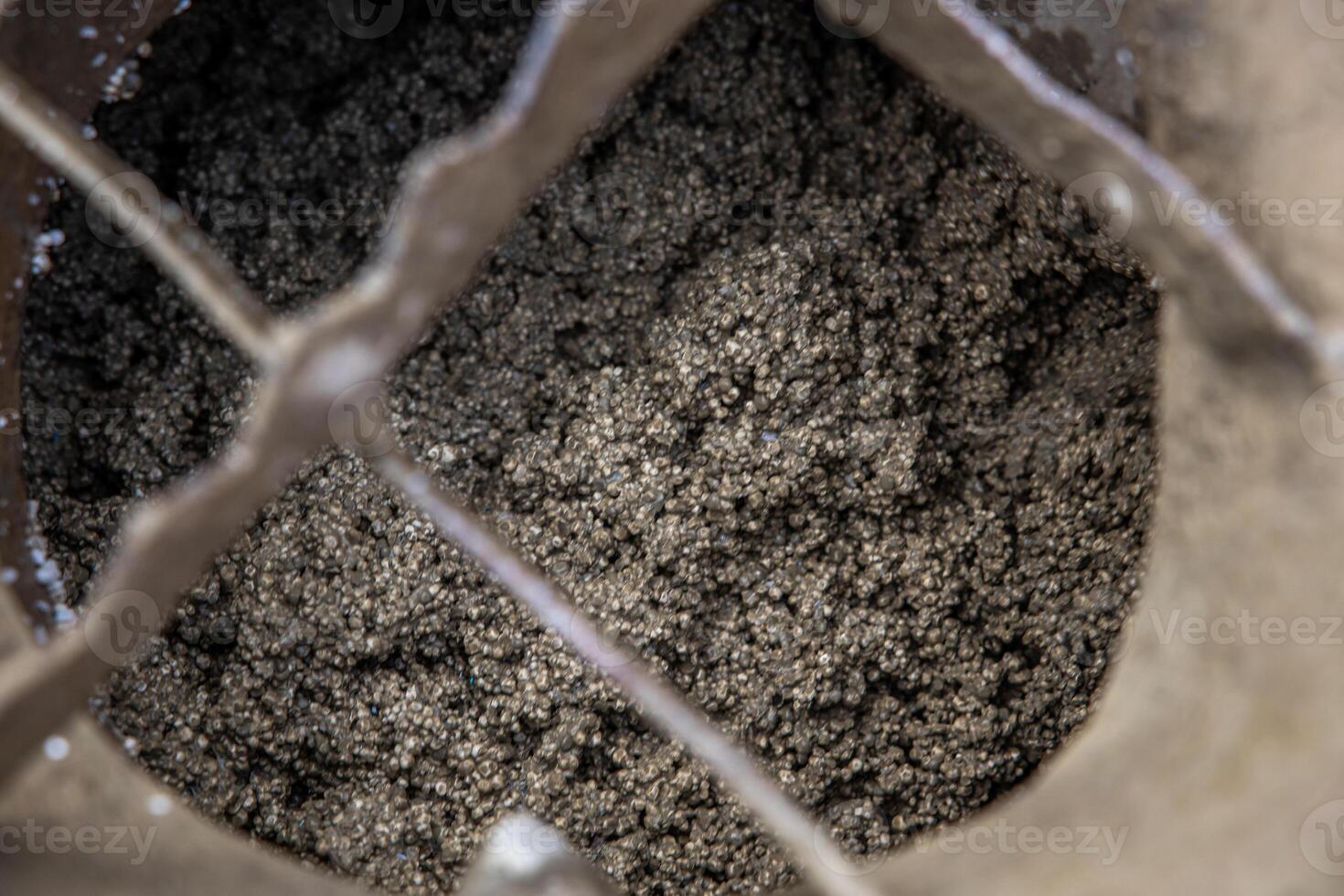 A detailed view of small metallic particles in a container, partially covered by a crisscross metal grate, highlighting texture and industrial design. photo